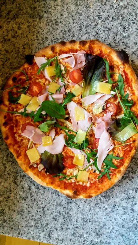 Pizza jambon et ananas, roquette et copeaux de fromage.