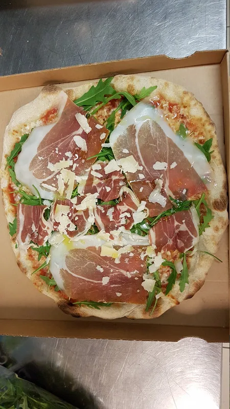 Pizza jambon cru, roquette et copeaux de parmesan, croûte au feu de bois.