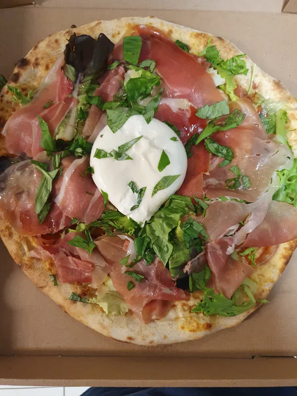 Pizza jambon cru, mozzarella crémeuse et salade, vue de dessus.